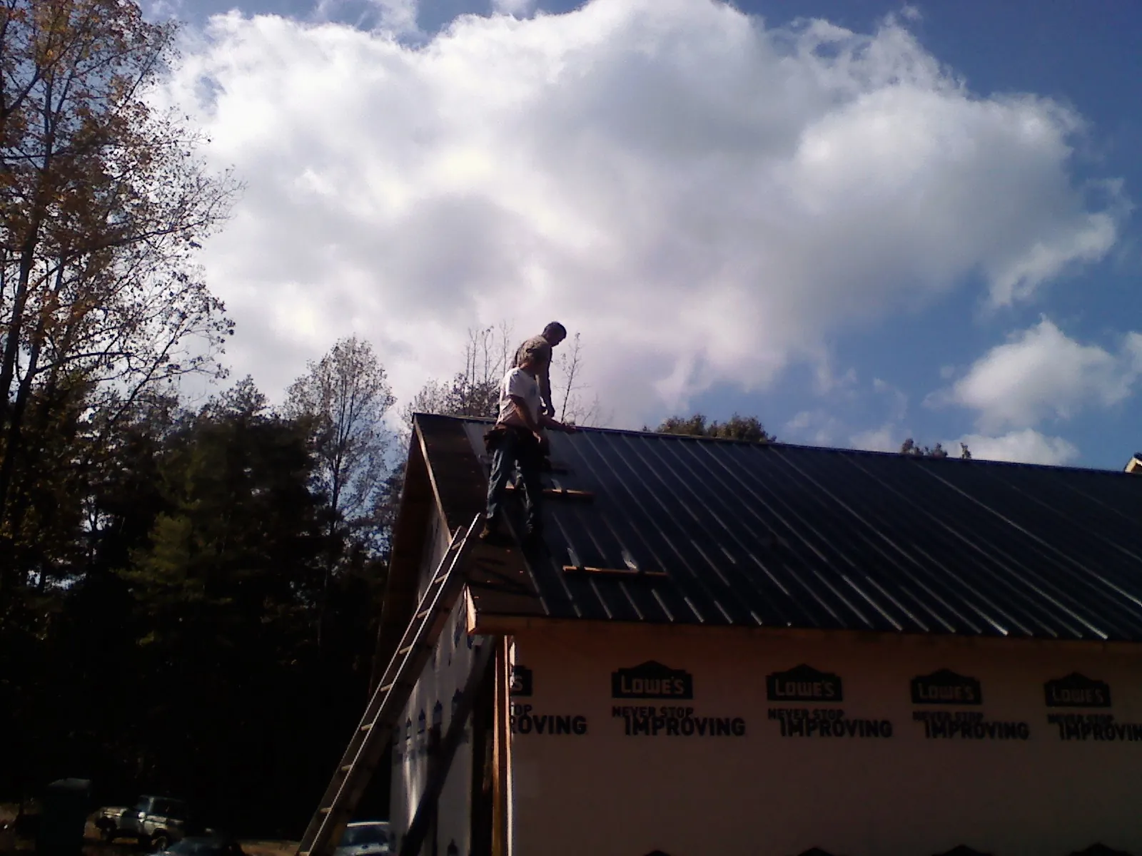 Roofer fastening dark metal panels high against a cloudy sky, from a Roof Inspection job in Wyoming